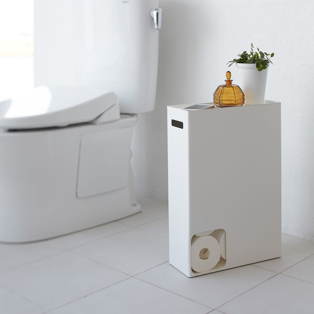 Vorderansicht des weißen Toilettenpapierhalters von Yamazaki Home mit Toilettenpapier und Dekorationsartikeln im Badezimmer.